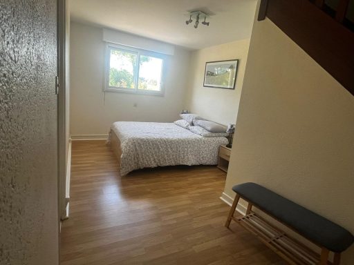 Chambre 1 : Lit double Chambre lumineuse avec un lit double, un banc en bois et des murs clairs.