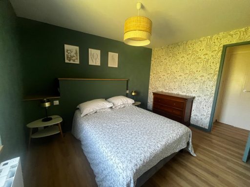 Chambre 3 : Lit double Chambre avec un lit double, murs verts, luminaire suspendu et décor floral.